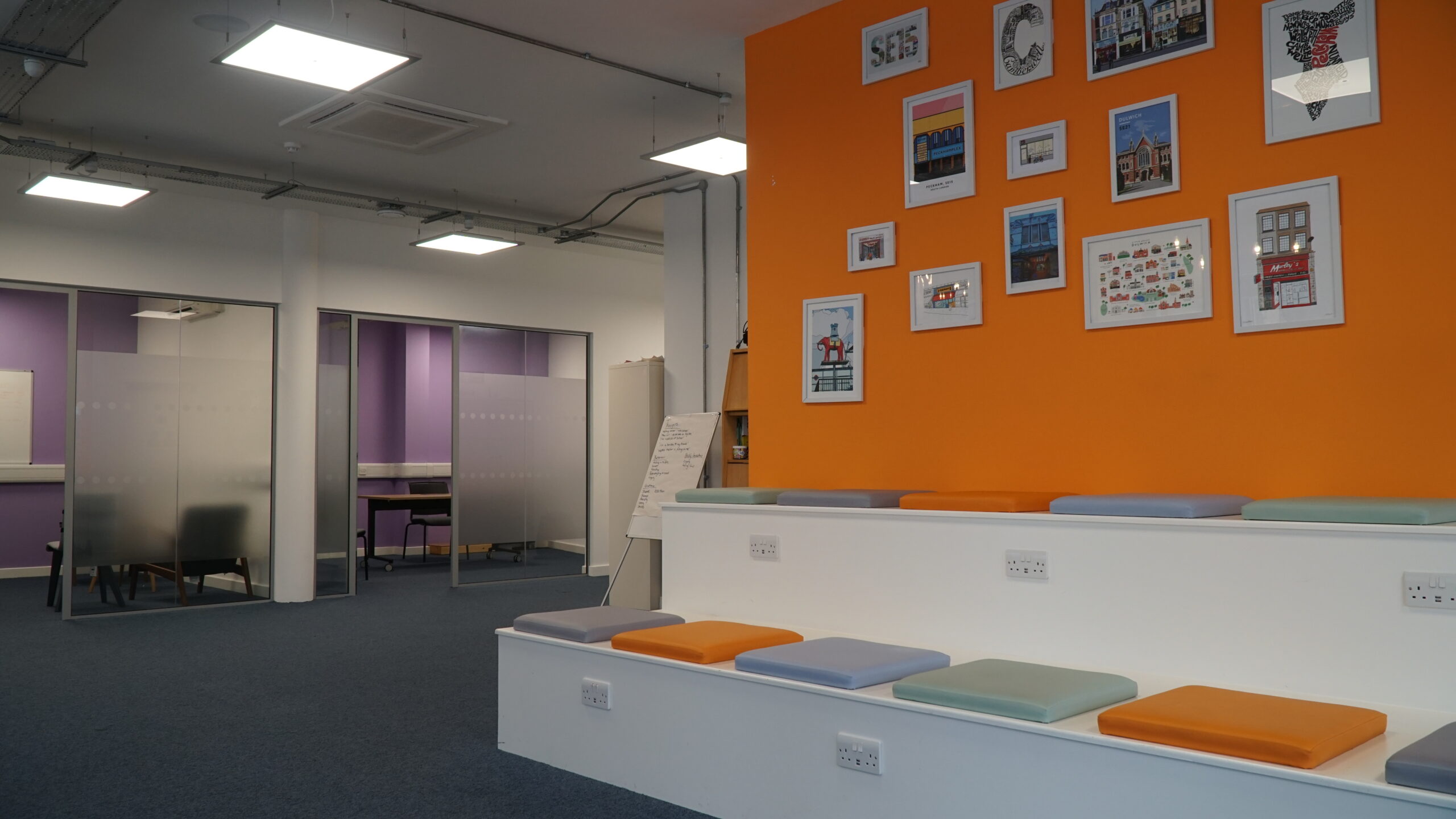 A spacious room with orange walls and artwork, leading up to two therapy rooms with purple walls. The rooms have a warm and inviting atmosphere.