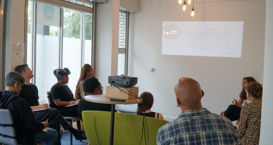 the nest's staff take part in training. here they are sat on green couches, looking at a projection on the wall.